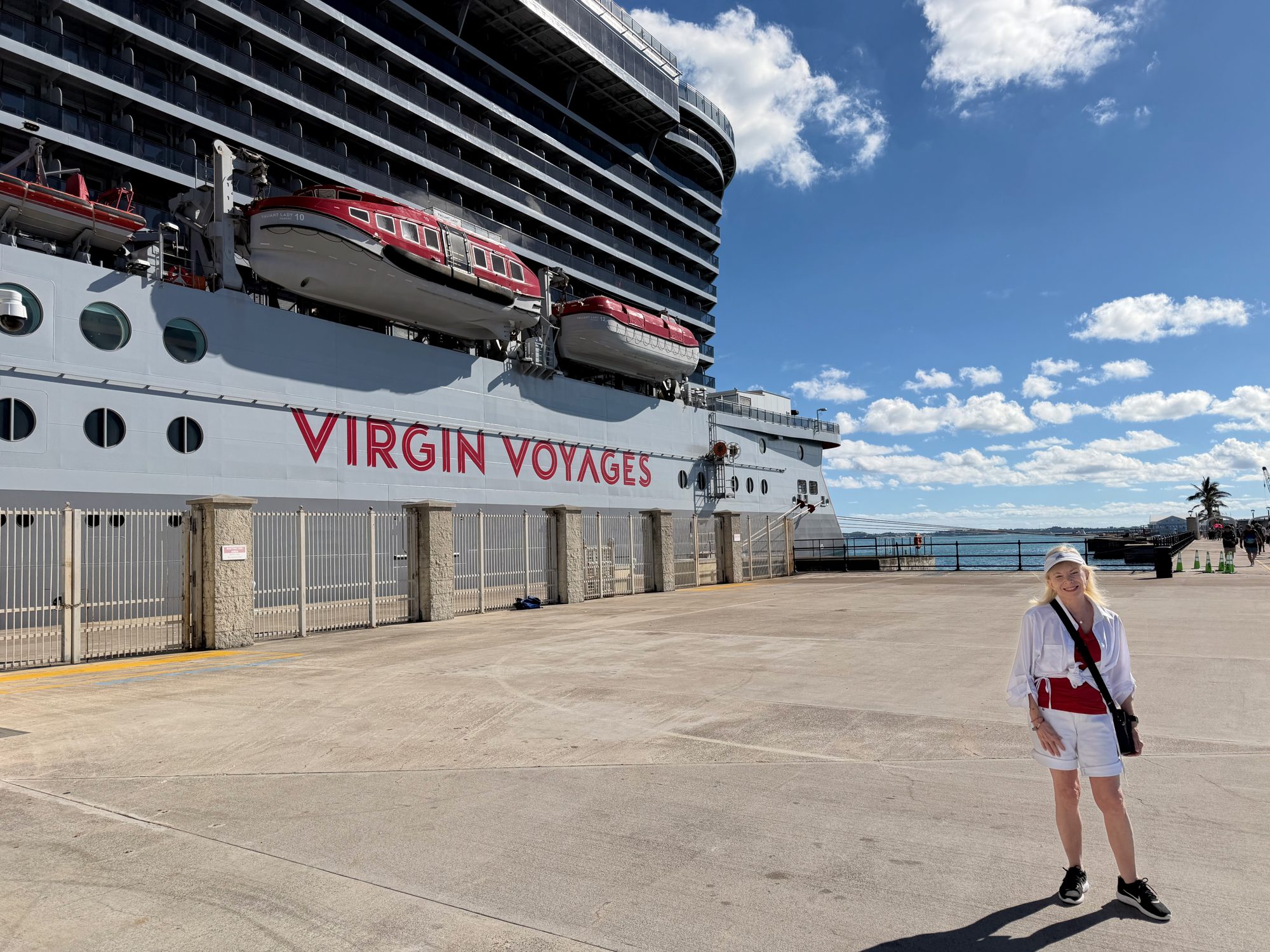 Dana Wallace Cash standing on the pier beside the hull of Valiant Lady, with Virgin Voyages lettered on the ship