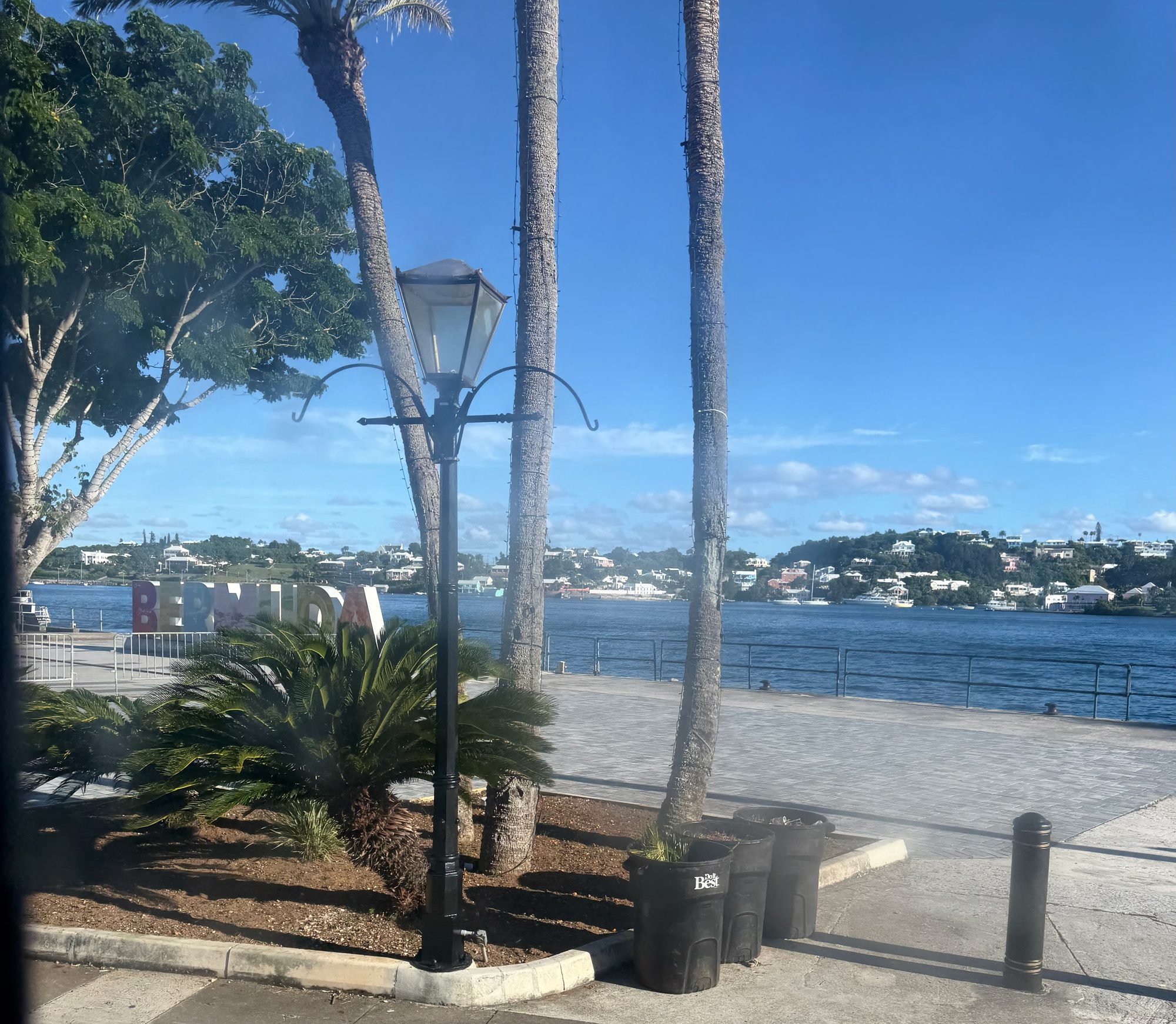 Palm trees and a waterfront promenade at the Dockyard, with a large Bermuda sign and pastel houses across the water