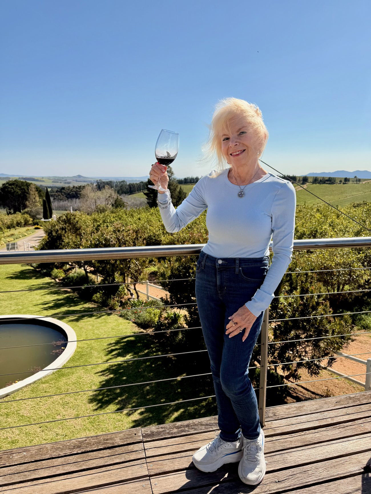 Dana Wallace Cash raising a glass of red wine on a terrace above vineyards