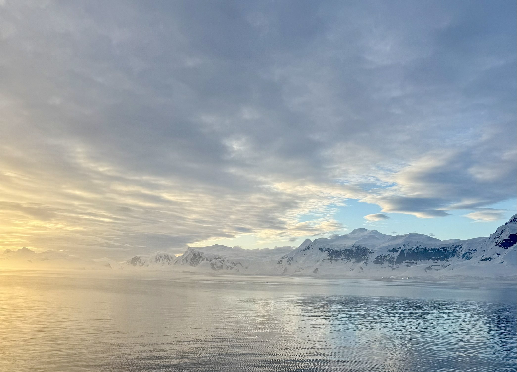 Low golden light across still water toward snow-covered Antarctic mountains