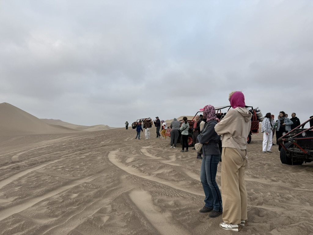 A group of travellers standing beside dune buggies on a broad sand slope