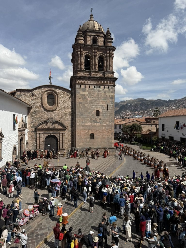 A procession in costume filling a stone plaza in Cusco, crowds watching from all sides