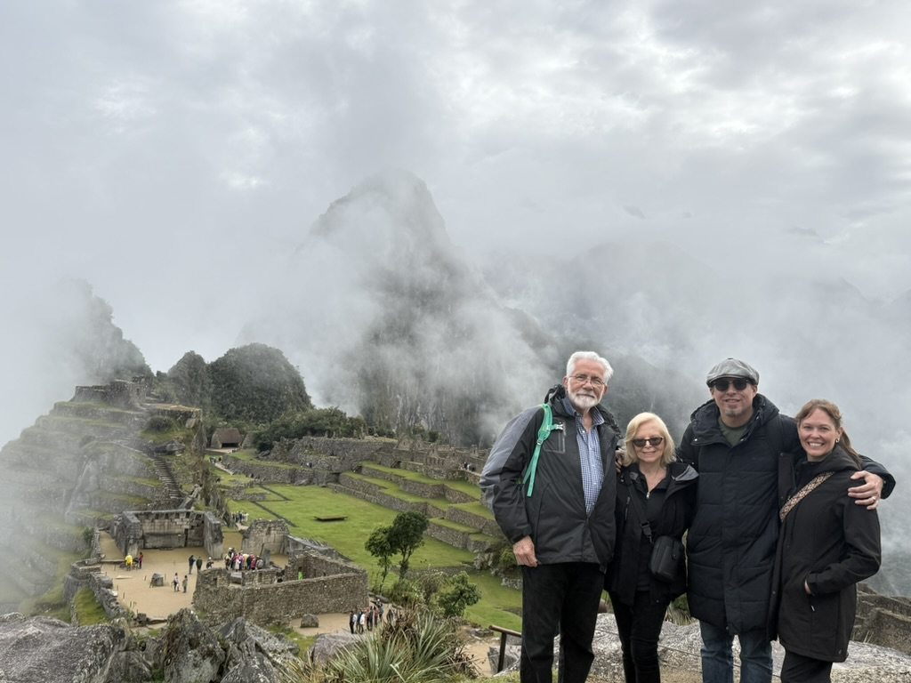 Four travellers on the viewpoint above Machu Picchu, Huayna Picchu wrapped in cloud behind them