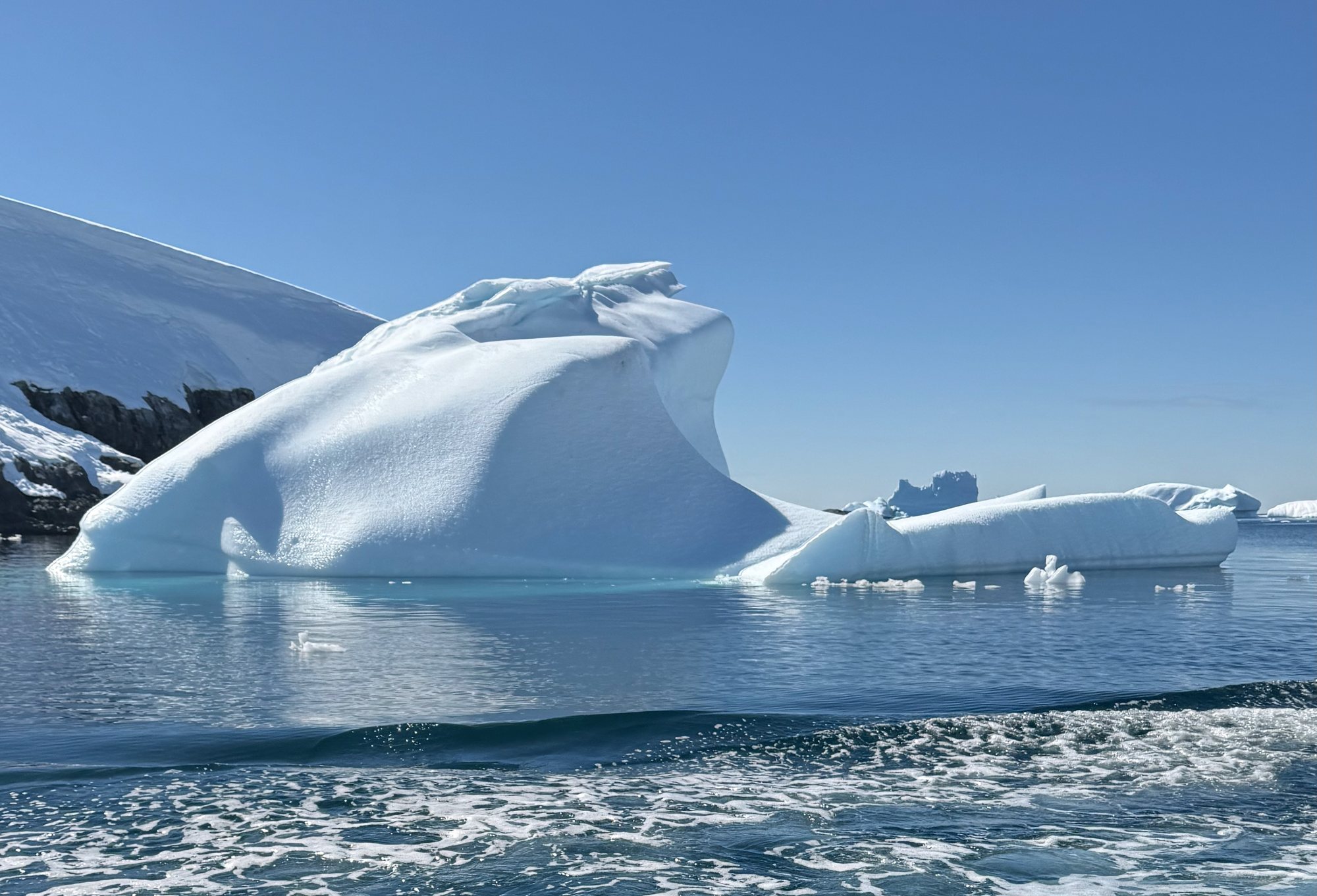 A sculpted white iceberg under a clear blue sky, dark rock behind it