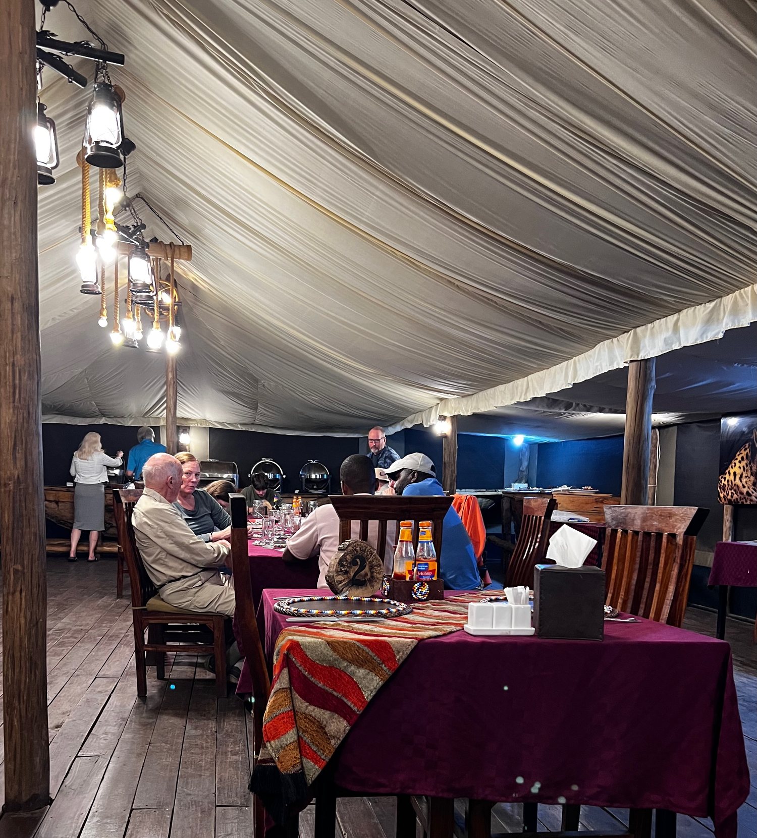 The interior of a tented camp dining room, lantern-lit, with laid tables under canvas